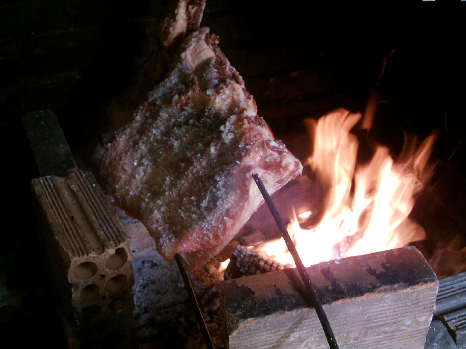 Large salted beef rib roasting on a skewer by an open fire