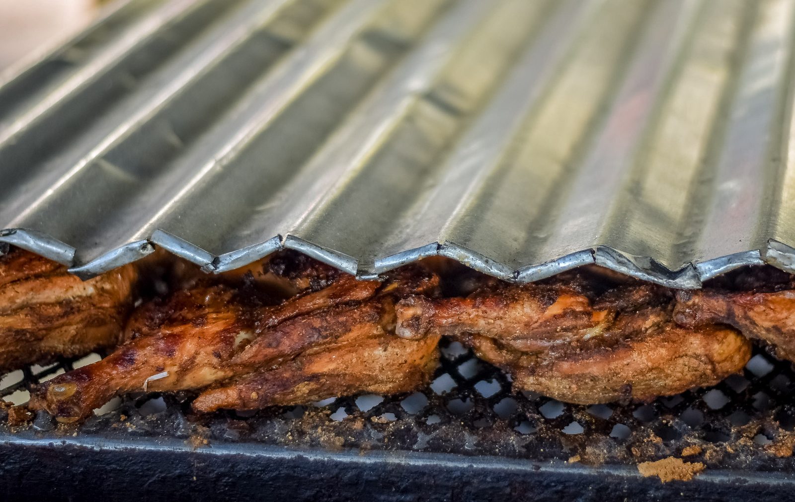 Jerk chicken cooking under a corrugated metal sheet