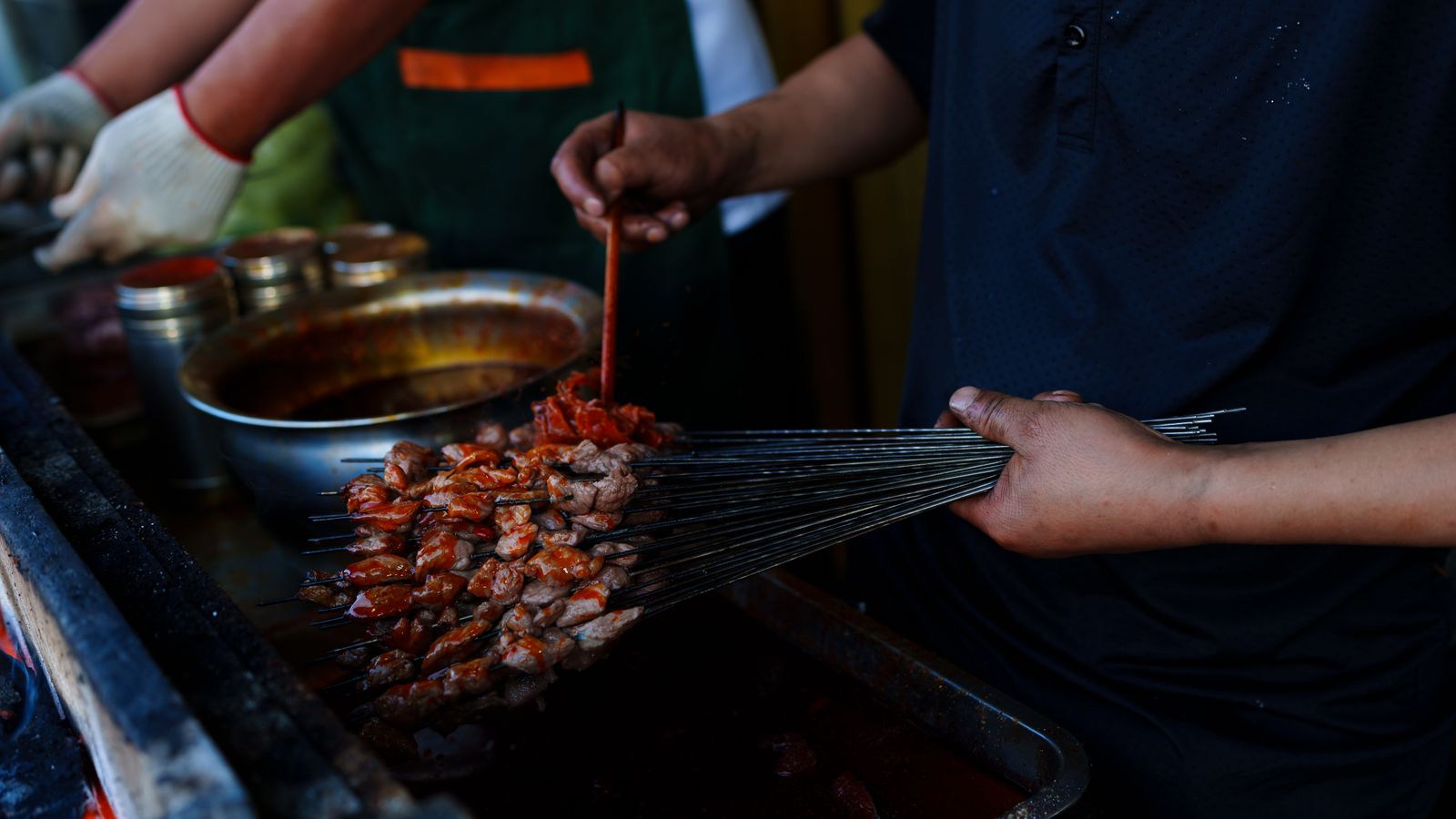 Vendor holding a fan of thin skewers of red-marinated lamb