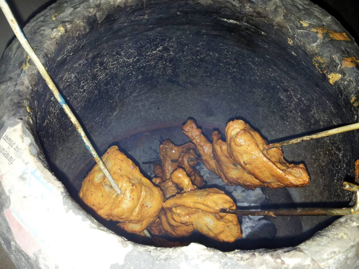 Marinated chicken on skewers inside a clay tandoor oven
