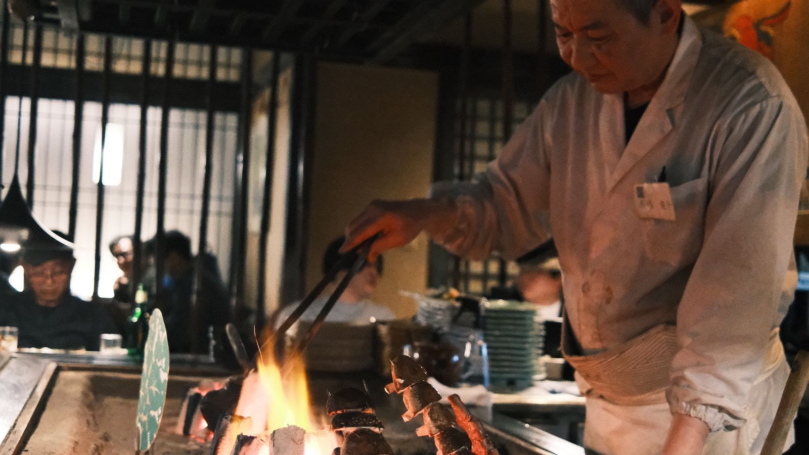 Chef grilling skewers over charcoal at a robata counter