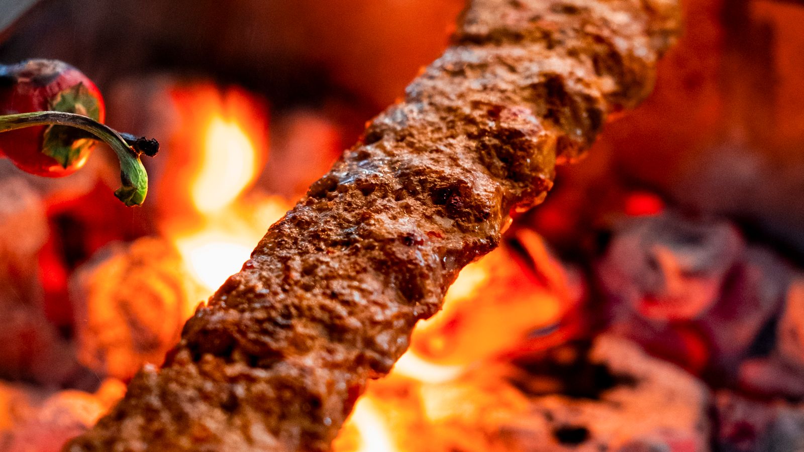 Long Adana kebab of minced meat over glowing charcoal